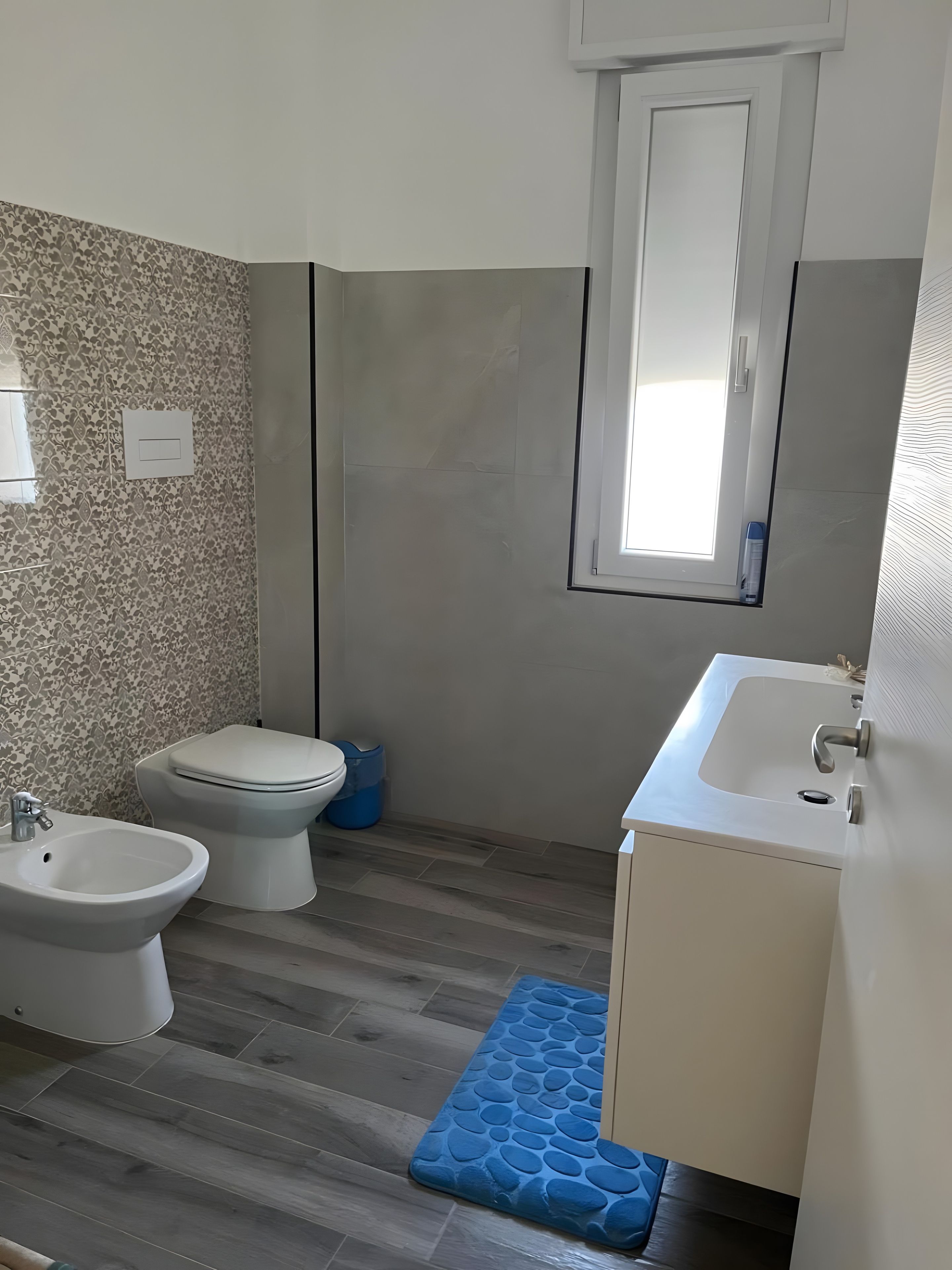 Ein Badezimmer mit Toilette, Bidet, Waschbecken und einem Fenster.