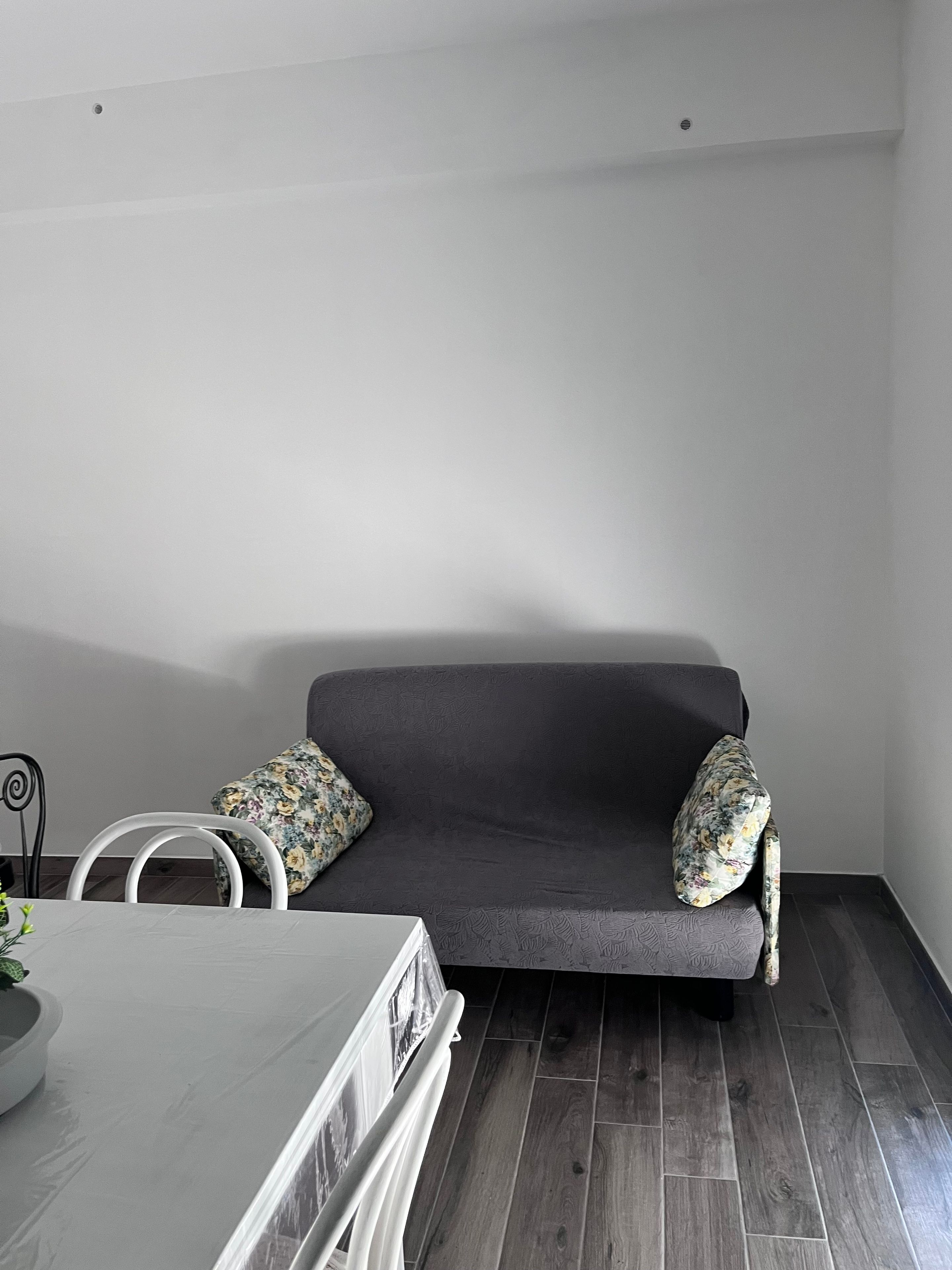 A modern living room with a grey sofa, two floral cushions, a white table, and a white chair.