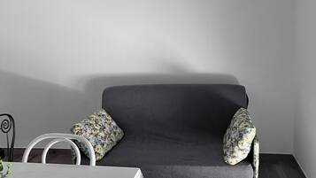 A modern living room with a grey sofa, two floral cushions, a white table, and a white chair.