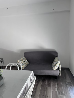 A modern living room with a grey sofa, two floral cushions, a white table, and a white chair. - Casa Del Giglio Apartment (Vigliatore)
