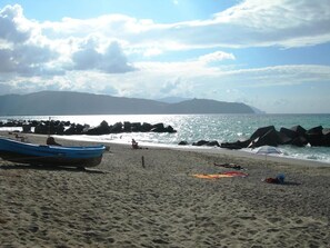 A beach with a boat, rocky shoreline, and distant mountains.