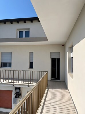 A modern building with a flat roof, a balcony with a metal railing, and a tiled floor.