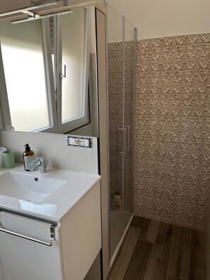 A bathroom with a white sink, a mirror, a glass shower enclosure, and patterned wall tiles. - Apartment 'Casa Del Giglio - MonoVerde' with Balcony and Air Conditioning (Vigliatore)