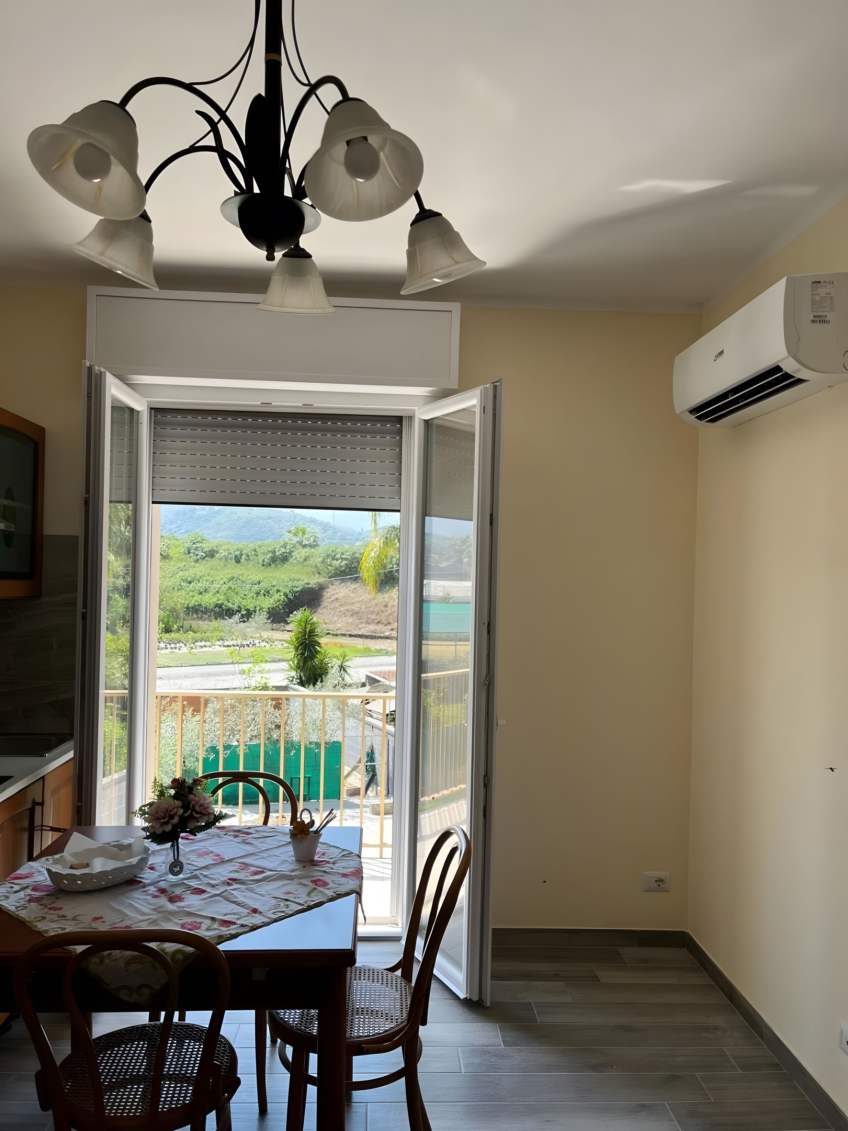 A balcony with a table and chairs, an air conditioning unit, and a view of greenery.