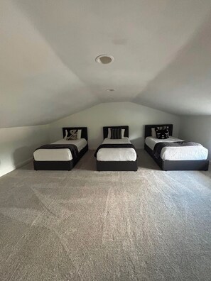 Ein Zimmer mit drei nebeneinanderstehenden Betten, einer geneigten Decke und einem Teppichboden.