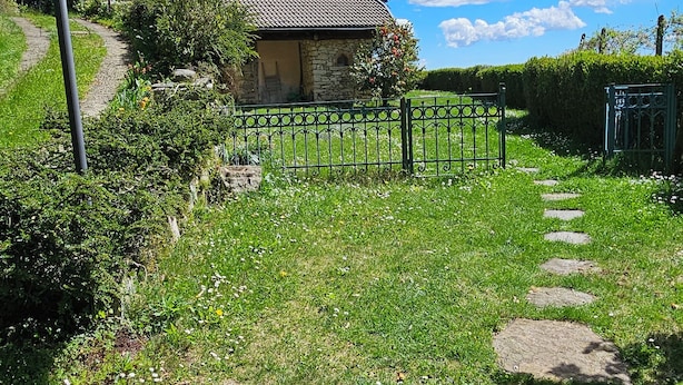 Een stenen huis met pannendak, omringd door een tuin met een geplaveid pad ernaartoe.