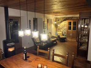 Ein gemütlicher Essbereich mit Holztisch, Stühlen, einer Weinflasche und Gläsern. Im Hintergrund ist eine Steinwand und eine Holztür zu sehen.