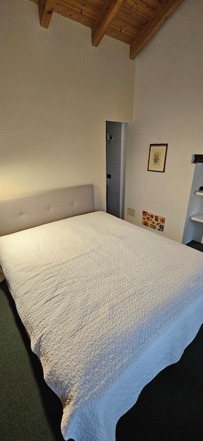 Une chambre avec un grand lit, un plafond en bois et une petite étagère fixée au mur.