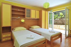 A bedroom with two single beds, wooden furniture, a small table, and a sliding glass door to a balcony. - Spacious 100m2 apartment with big terrace & great sea view (Slatine)