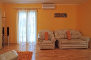 Uma sala de estar com sofá e poltrona, televisão e janela com cortinas.