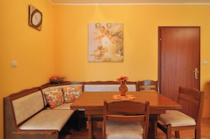 A dining area with a wooden table, chairs, a bench with floral cushions, a vase with flowers, a clock, and a door. - Spacious 100m2 apartment with big terrace & great sea view (Slatine)
