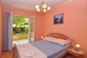 Un dormitorio con cama, mesita de noche, lámpara, un cuadro y vistas a un jardín por un ventanal corredero.
