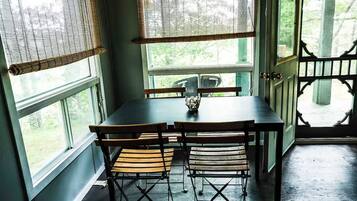 A dining area with a table and chairs, a vase on the table, and a view through a door.