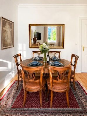 Une salle à manger avec une table ronde, six chaises, un vase de fleurs et un grand miroir au mur.