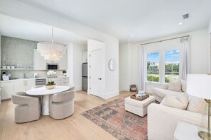 A modern kitchen with a dining area, a living room with a sofa and a coffee table, and a large window with a view. - Just B | Private Pool | Pickleball Court | Home Gym (Inlet Beach)