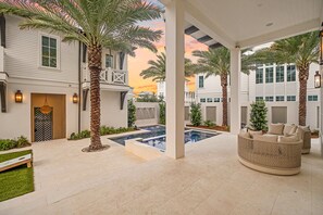 A covered outdoor area with a pool, palm trees, and a seating area with cushions. - Just B | Private Pool | Pickleball Court | Home Gym (Inlet Beach)