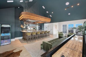 A modern kitchen with bar stools, a green sofa, and a view of the city. - Just B | Private Pool | Pickleball Court | Home Gym (Inlet Beach)