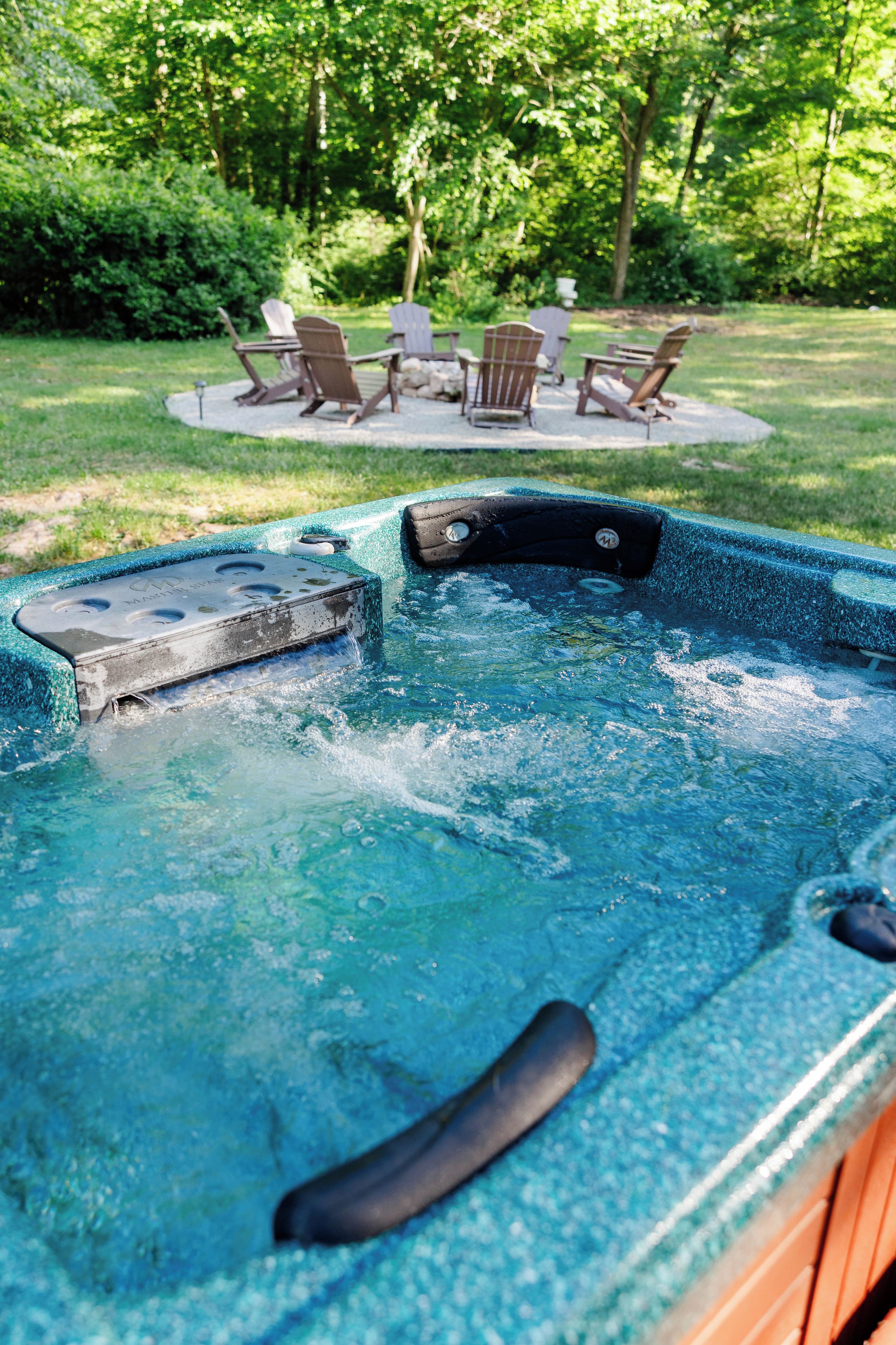 A hot tub with a built-in seat and a control panel, surrounded by a grassy area with outdoor furniture.
