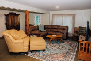 A living room with a brown leather sofa, a yellow armchair, a wooden coffee table, and a patterned rug. - Cabin with hot tub, internet, path to the creek, 4 acres in peaceful Landisburg (Landisburg)