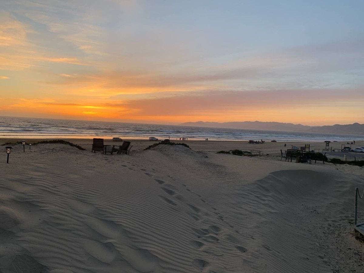 Una playa con dunas de arena, algunas sillas y una torre de salvavidas a lo lejos.