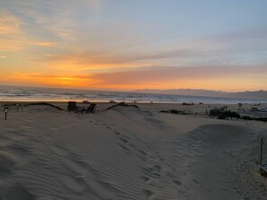 Ein Strand mit Dünen, einigen Liegestühlen und einem Rettungsturm in der Ferne.
