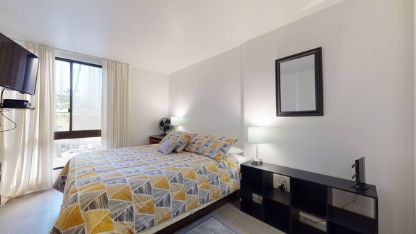 Een slaapkamer met een bed, nachtlampjes, een televisie en een spiegel.