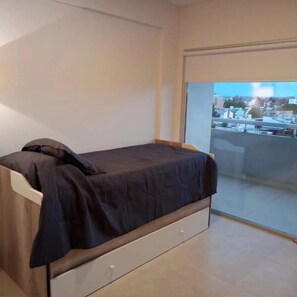 A small, single-bed room with a view of a cityscape through a sliding glass door. - Comfort and relaxation (Puerto Madryn)