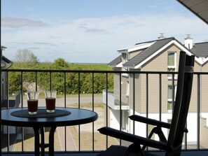 A balcony with a table and two glasses of a beverage, overlooking a residential area with houses and a clear sky. - House No. 34, Holiday Home Fischerhus (Wangerland)