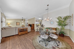 A spacious living room with a sofa, a dining table with chairs, a ceiling fan, and a chandelier. - 2472 Z3A Village of Lynnhaven (The Villages)