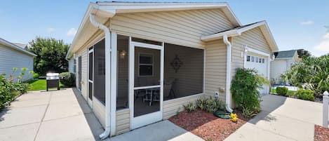 A single-story house with a covered porch, a visible garage door, and a small garden area with mulch and plants.