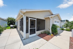 A single-story house with a covered porch, a visible garage door, and a small garden area with mulch and plants. - 2472 Z3A Village of Lynnhaven (The Villages)