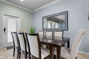 A dining area with a rectangular table, six chairs, a potted plant, and a large mirror on the wall. - Resort Escape Near Disney: Poolside Family Fun! (Kissimmee)
