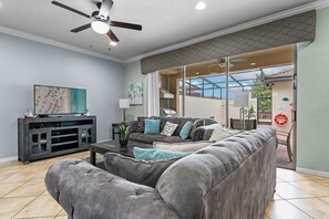 A living room with a grey sofa, a coffee table, a TV on a cabinet, and a ceiling fan. - Resort Escape Near Disney: Poolside Family Fun! (Kissimmee)