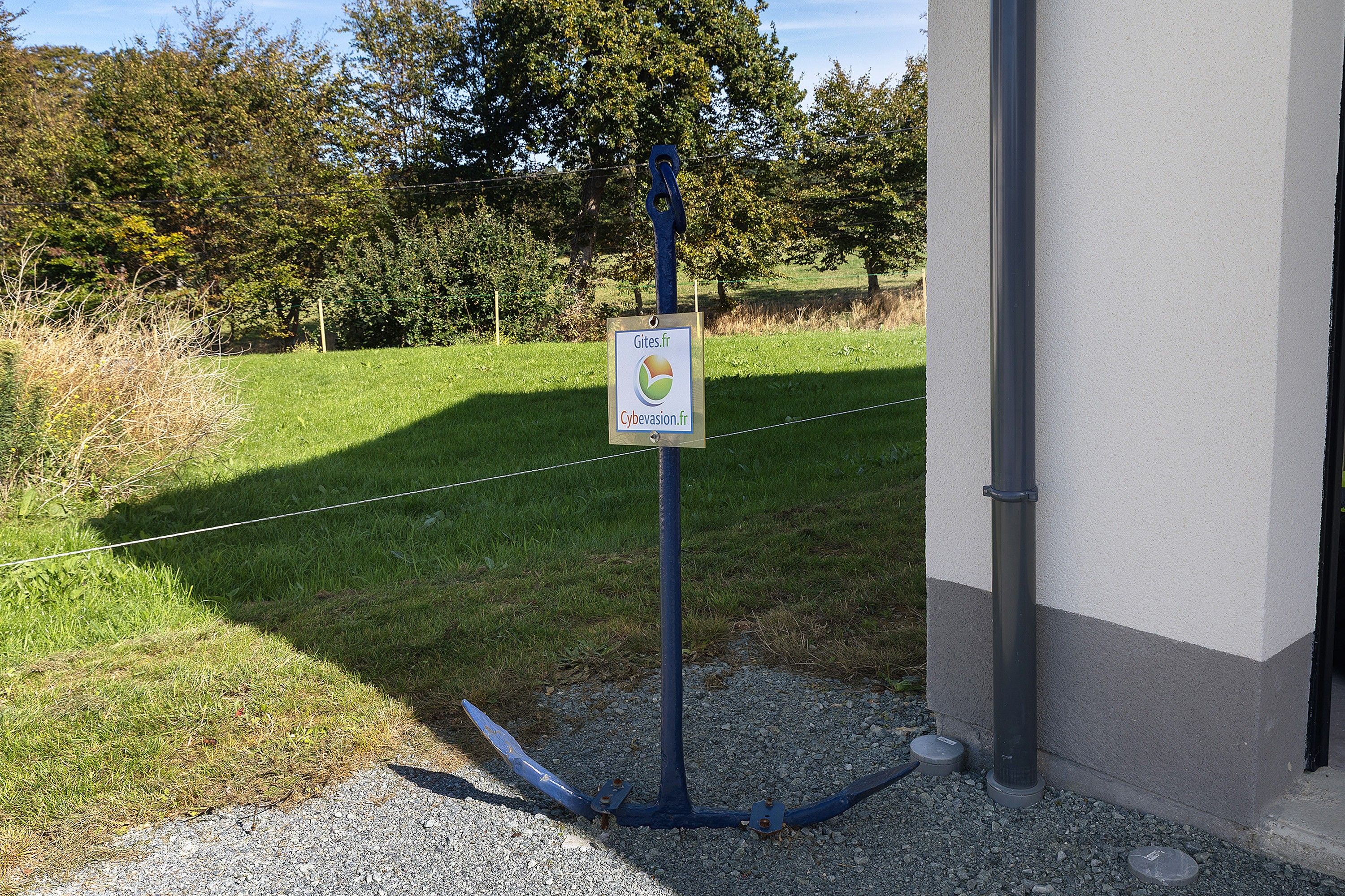 Un panneau d’affichage fixé à un poteau dont la base est recouverte de gravier, le tout se dressant sur un fond de champ herbeux et d’arbres.
