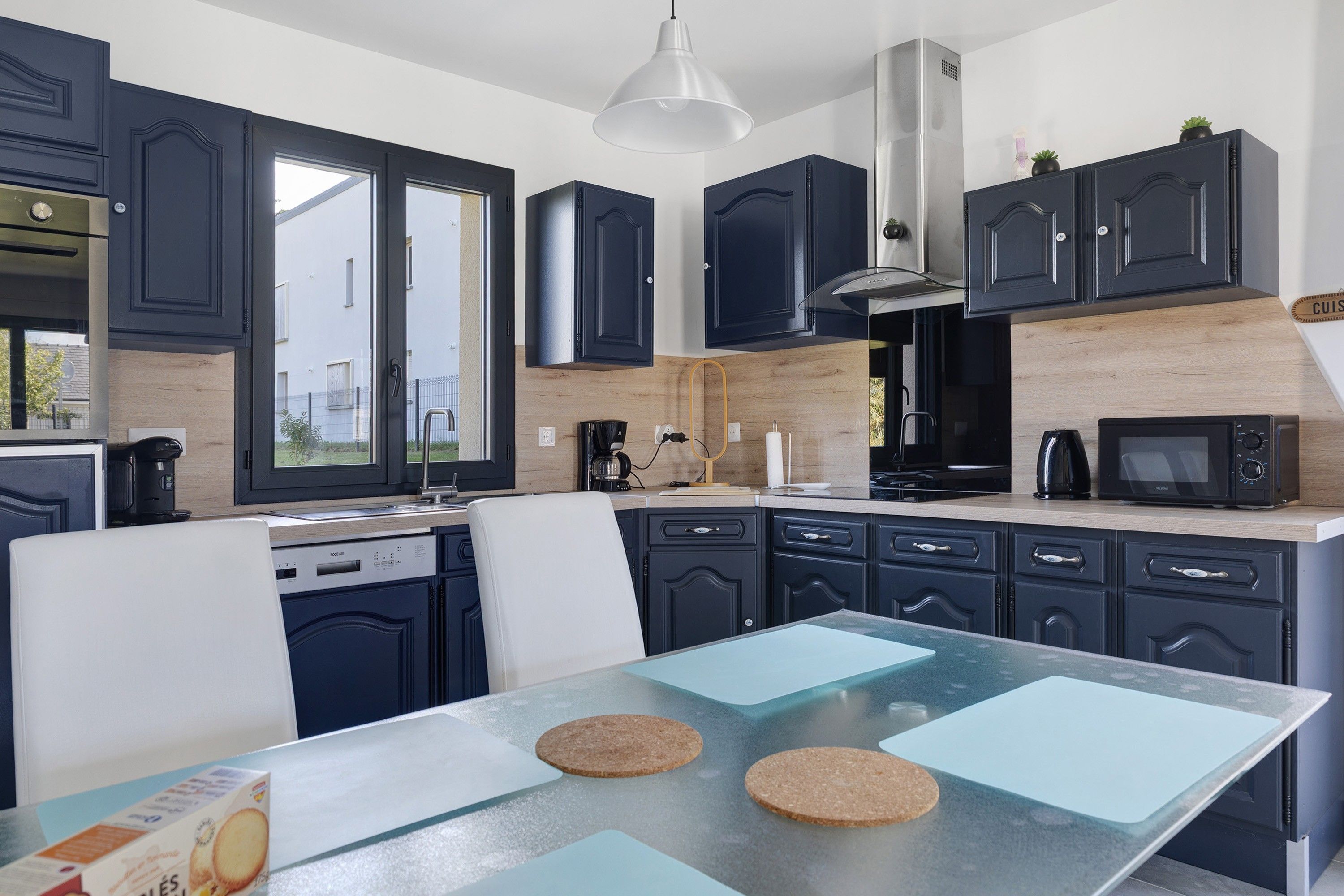 Une cuisine moderne avec des meubles de couleur sombre, une hotte en acier inoxydable et un coin repas doté d’une table en verre.