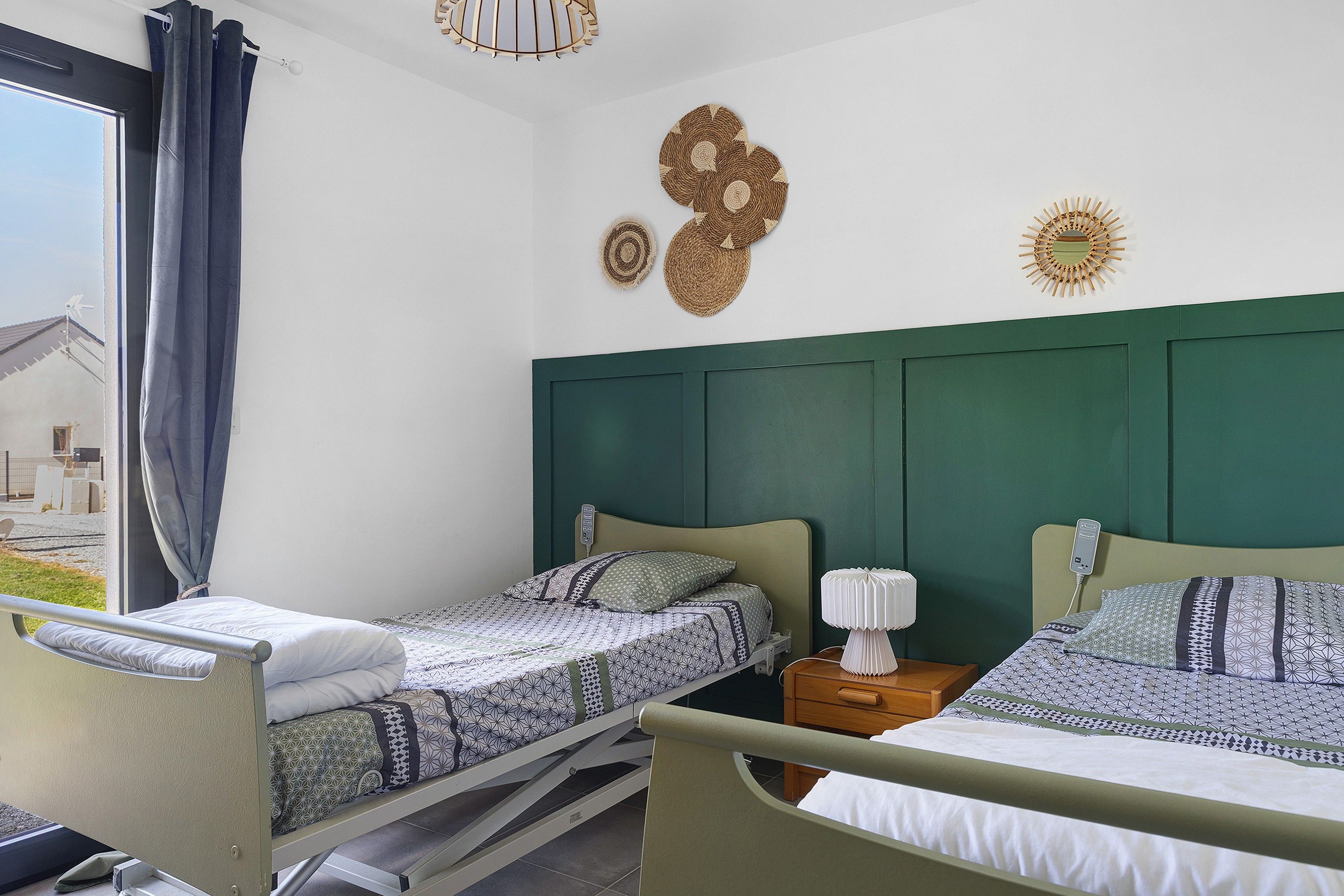 Une chambre avec deux lits, une fenêtre avec des rideaux et une vue sur une maison à l’extérieur.
