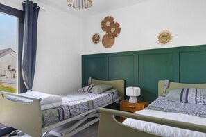 Una habitació amb dos llits, una finestra amb cortines i vista a una casa a l'exterior.
