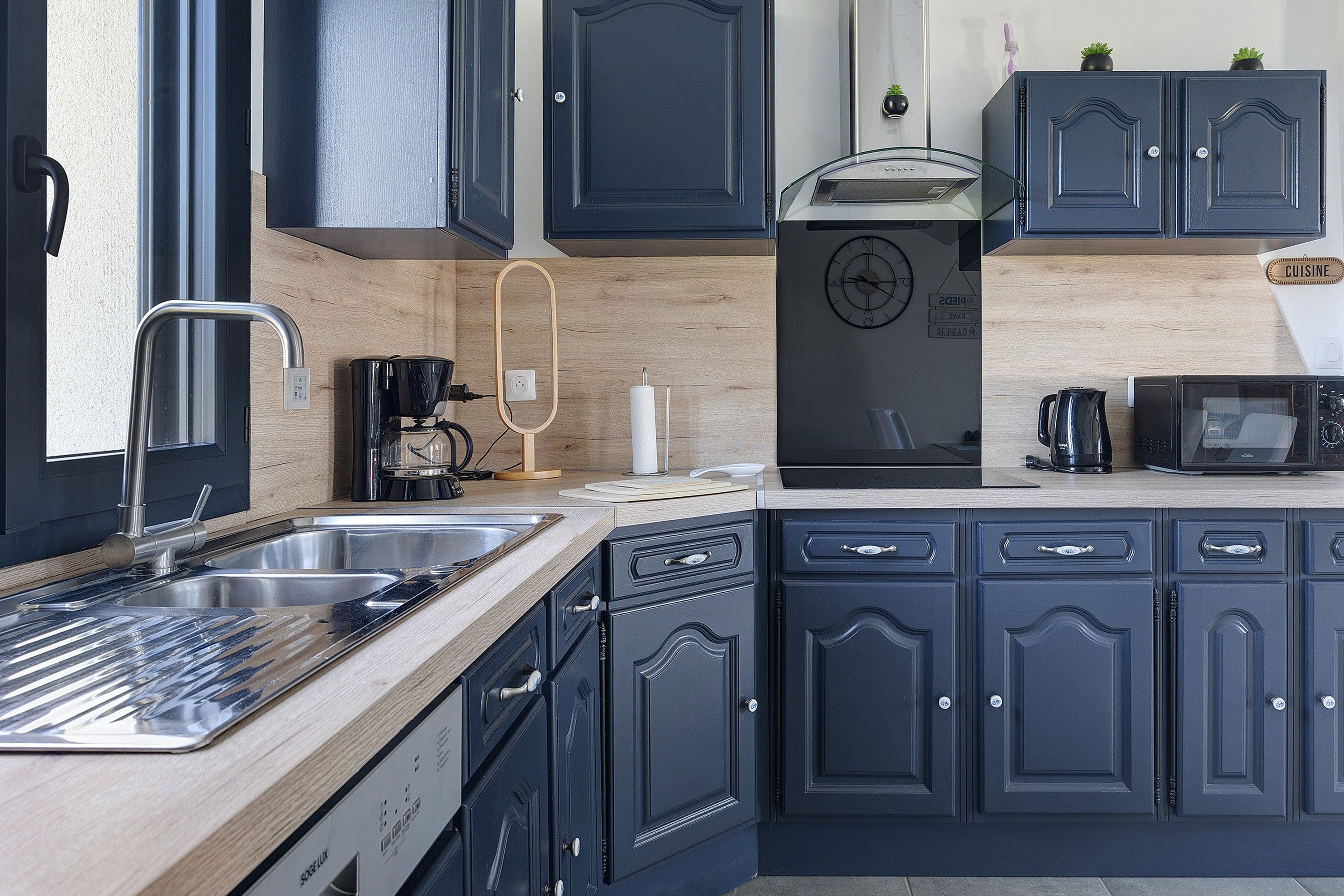 Une cuisine moderne avec des meubles de couleur sombre, des appareils électroménagers en acier inoxydable et un plan de travail en bois.
