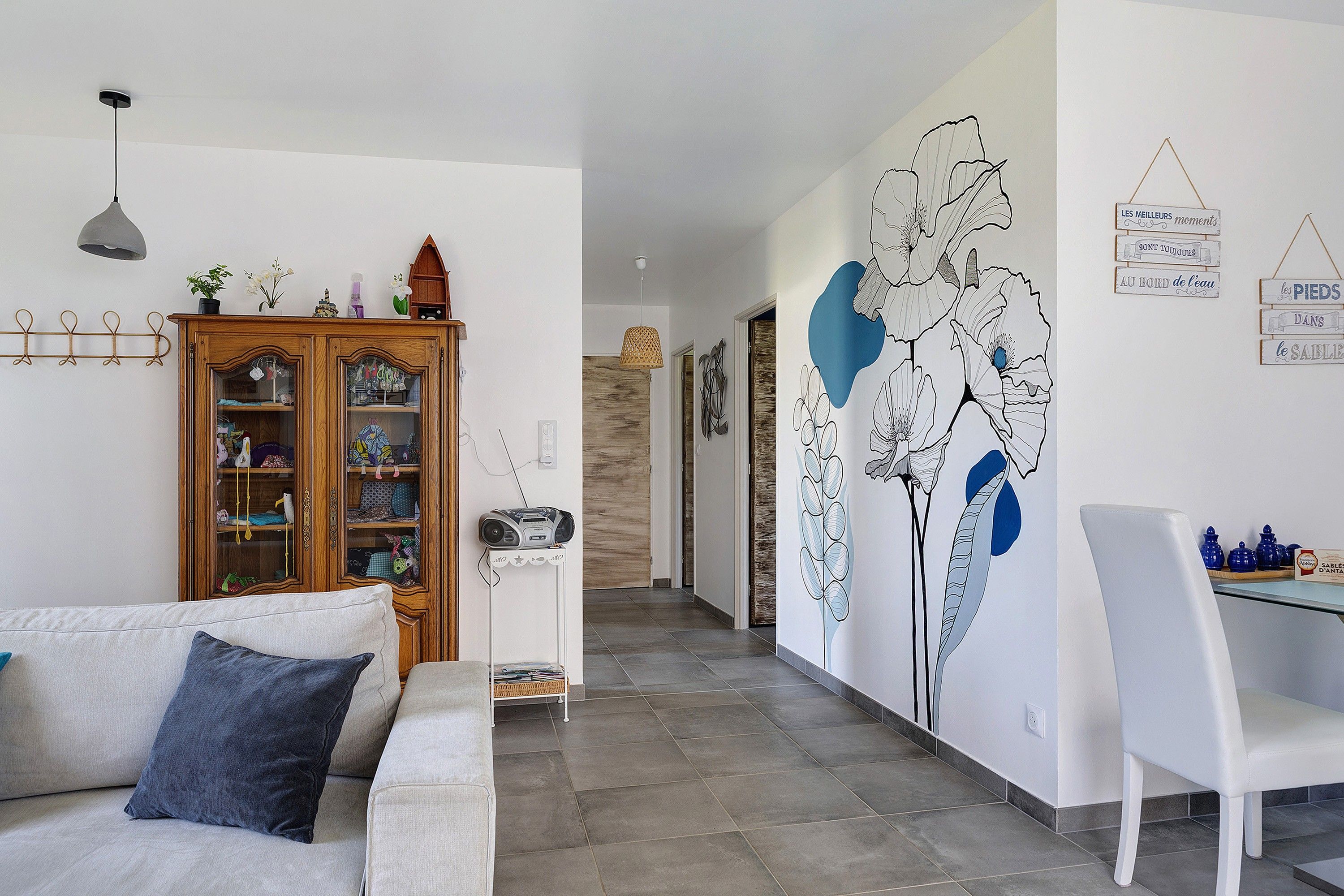 Un salon comprenant un canapé, un meuble et un mur orné d’une fresque à motifs floraux.