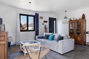 Een woonkamer met een bank, een salontafel, een rieten stoel, een kast en een raam met gordijnen.