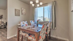 A dining area with a wooden table and chairs, a chandelier, and a window with curtains. - Family-Friendly 3BR | Dream Kids’ Room & Garage (Rapid City)