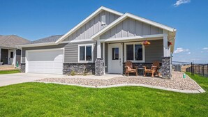A single-story house with a garage, a front porch with two chairs, and a stone accent wall. - Family-Friendly 3BR | Dream Kids’ Room & Garage (Rapid City)