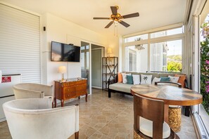 A well-lit living area with a ceiling fan, a flat-screen TV, a dining table, and a sofa with cushions. - Denize Sıfır Villa. Özel Plaj&Doğal Havuz.Bodrum (Milas)