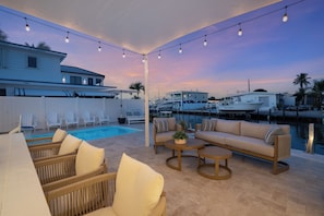 Área da piscina com mobiliário de exterior, vista para a marina e luzes de corda.