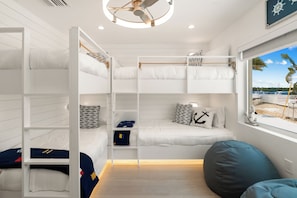 Quarto com beliches e vista para o mar, ventilador de teto e janela com vista para barcos.