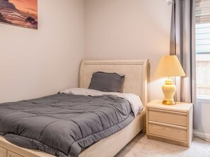 A bedroom with a bed, a bedside table with a lamp, a nightstand, and a window with blinds. - Woodridge - Entire Home (Porter)