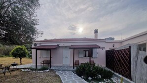 Una casa de planta baixa amb teulada de rajola, un porxo d'entrada amb dues cadires, un petit jardí amb un cactus i un camí pavimentat que condueix a la porta.