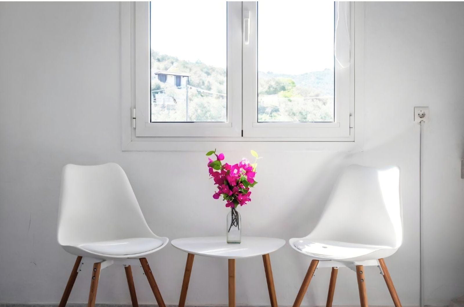 Une pièce avec deux chaises blanches et une petite table sur laquelle est posé un vase de fleurs.