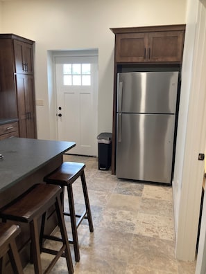 A kitchen with a stainless steel refrigerator, wooden cabinets, a white door, and a tiled floor.