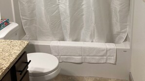 Un bagno con tenda da doccia bianca, un water bianco e un piano di lavoro in granito.